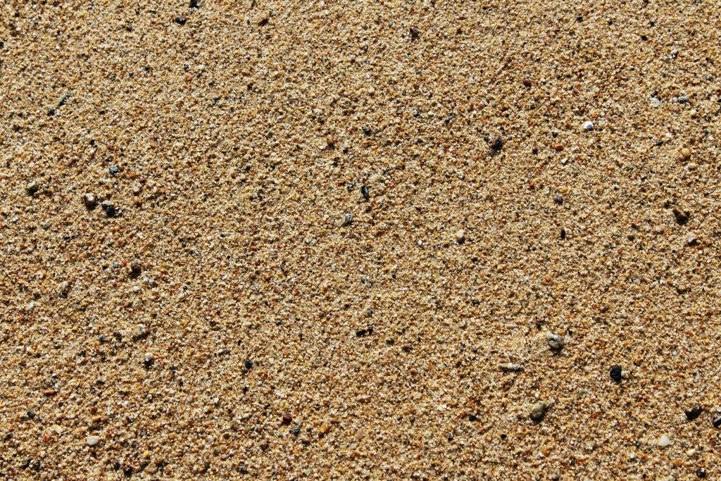 Detailed close-up of sandy beach surface displaying texture and tiny pebbles.
