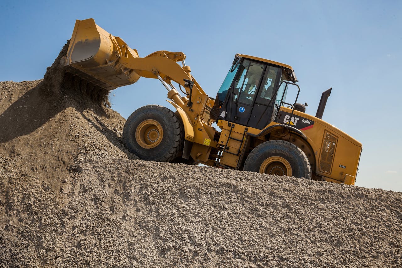 A yellow front loader moving gravel at a quarry under a blue sky.